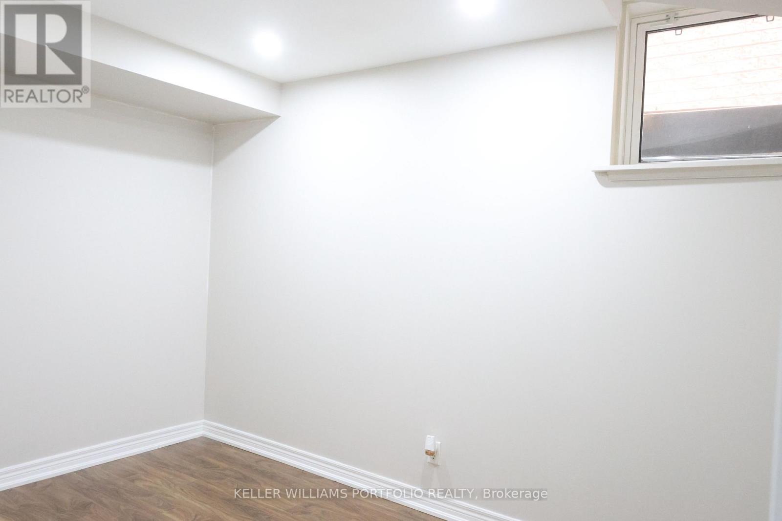 A white wall with a window and a wooden floor.