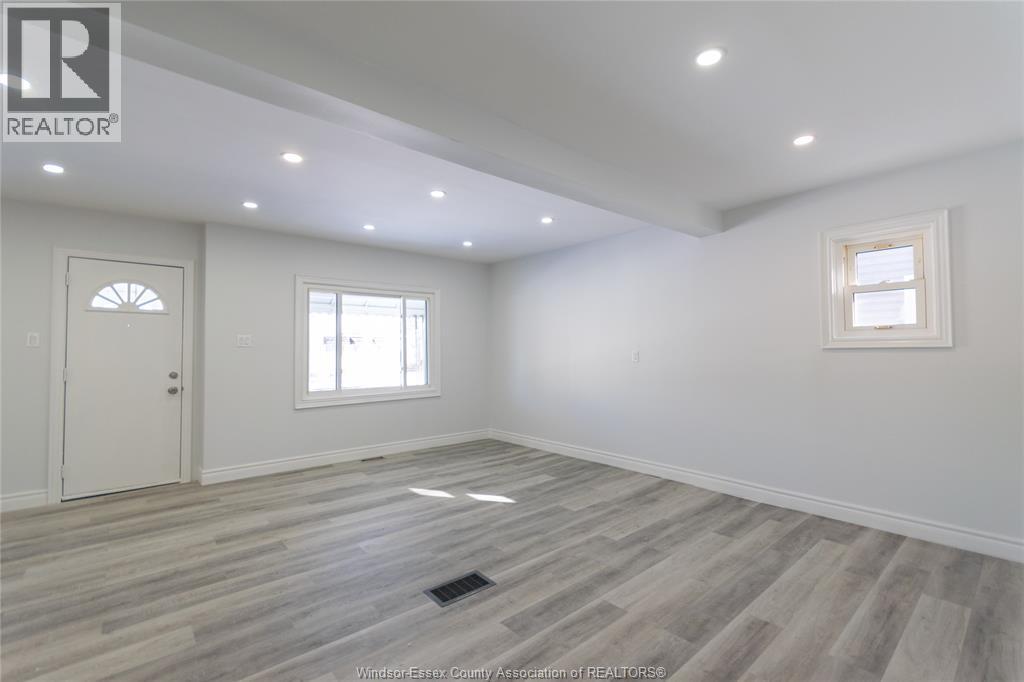 A spacious room with wooden flooring and two windows.