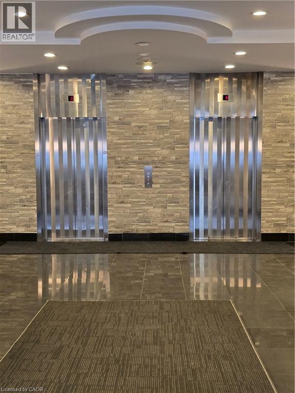 A hallway with a stone wall and two metallic doors.
