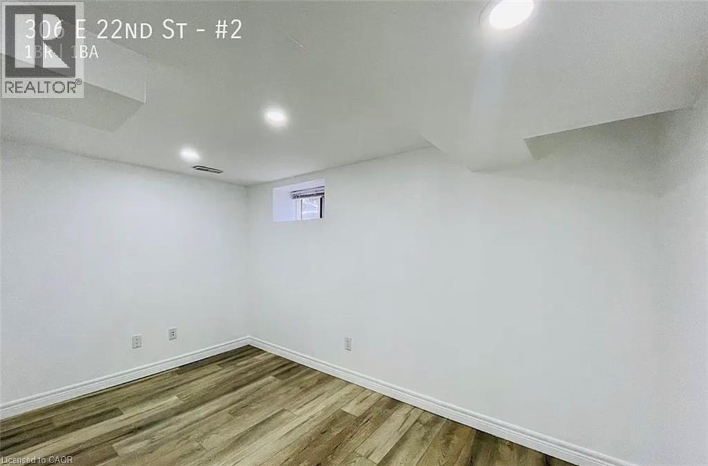 A room with wooden flooring and white walls, with a window on the wall.