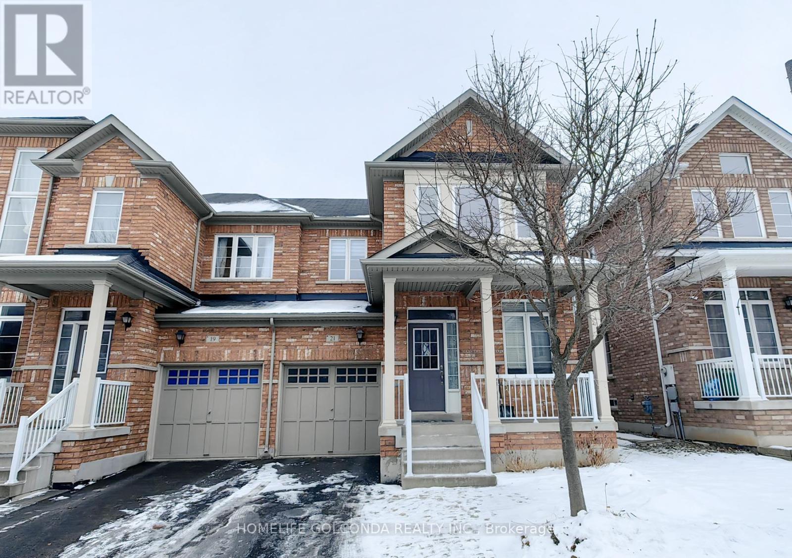 A large brick house with a garage and a tree in front.