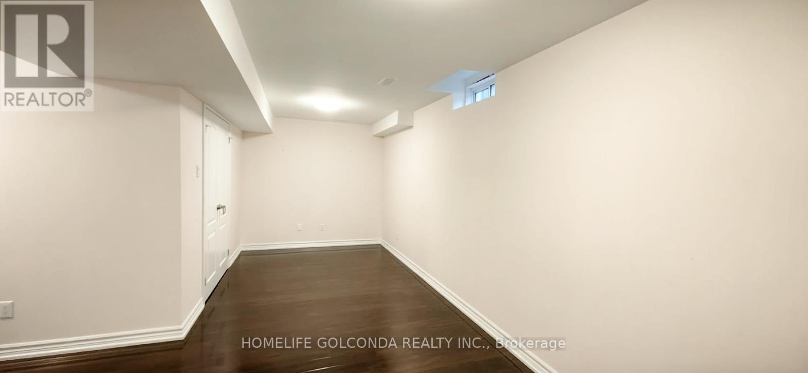 A spacious room with wooden floors and white walls, likely a living space.