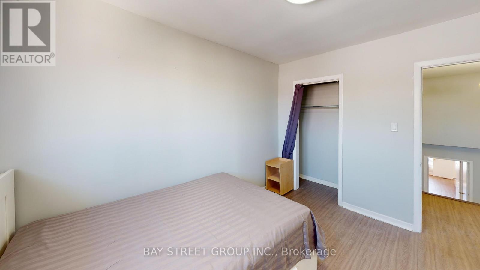 A bedroom with a bed, a nightstand, and a window with a view of the hallway.