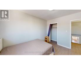 A bedroom with a bed, a nightstand, and a window with a view of the hallway.
