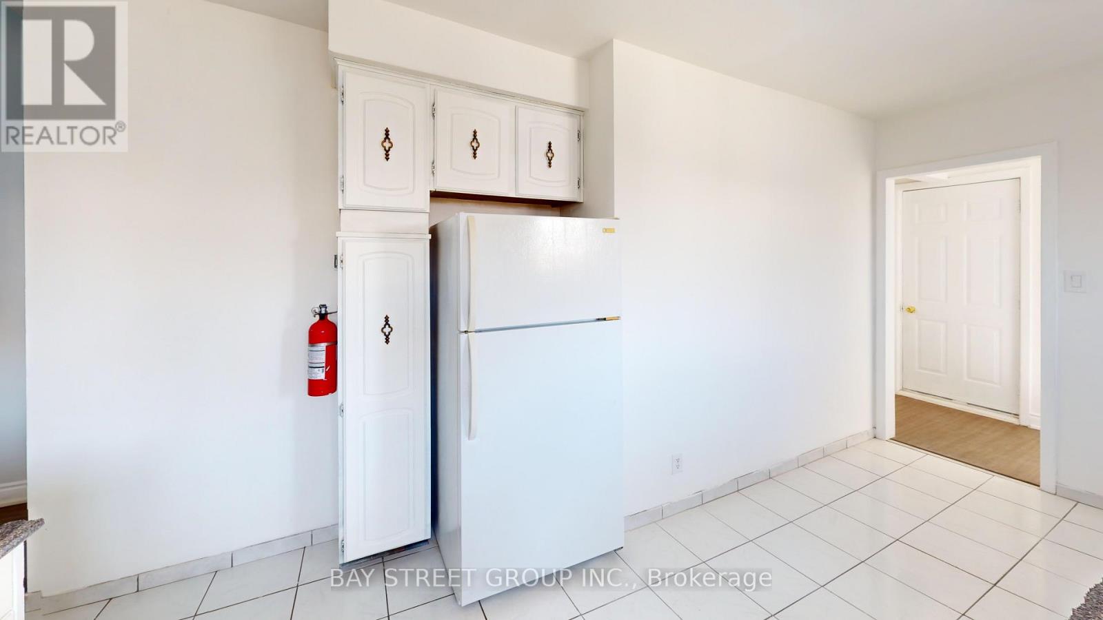 A white kitchen with a refrigerator, cabinets, and a fire extinguisher.