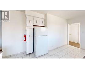 A white kitchen with a refrigerator, cabinets, and a fire extinguisher.