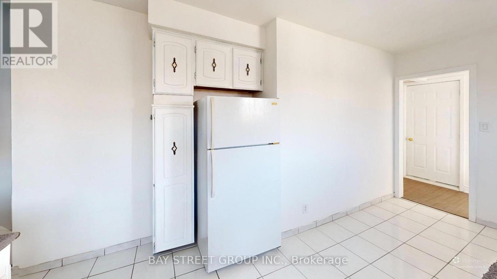 A white refrigerator in a kitchen with white cabinets.