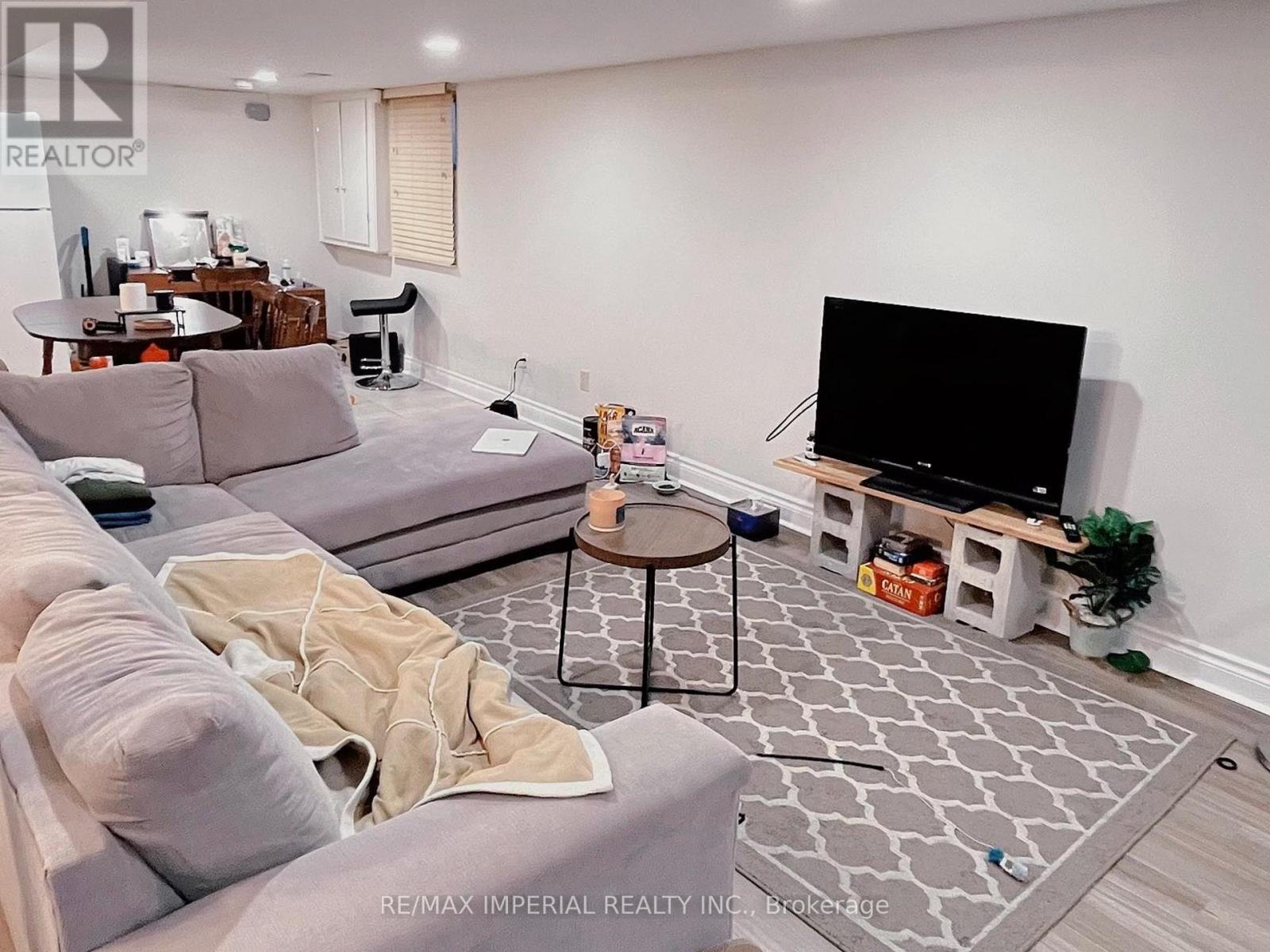 A living room with a grey couch, a black TV, and a grey and white patterned rug.