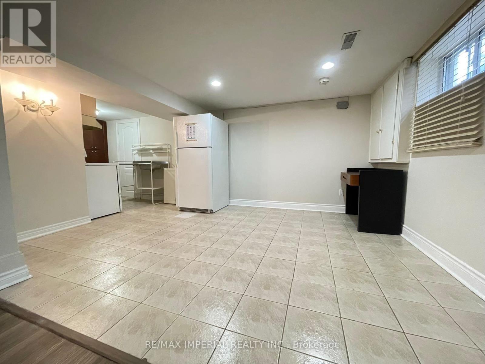 A spacious room with a tile floor and a refrigerator in the corner.