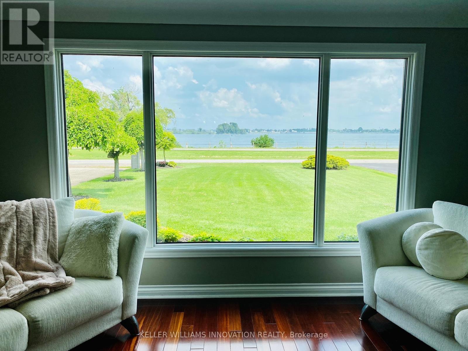 A living room with two couches and a view of a green field and water through the windows.
