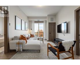 A bedroom with a bed covered in a blanket and pillows, a chair with a white furry cushion, and a flat-screen TV mounted on the wall.