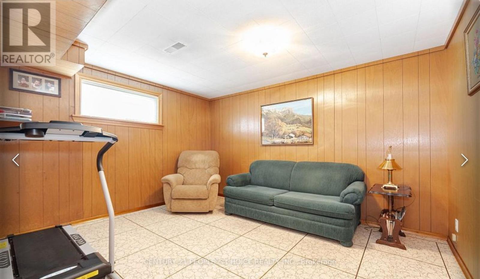 A living room with a green couch, a brown armchair, and a treadmill.
