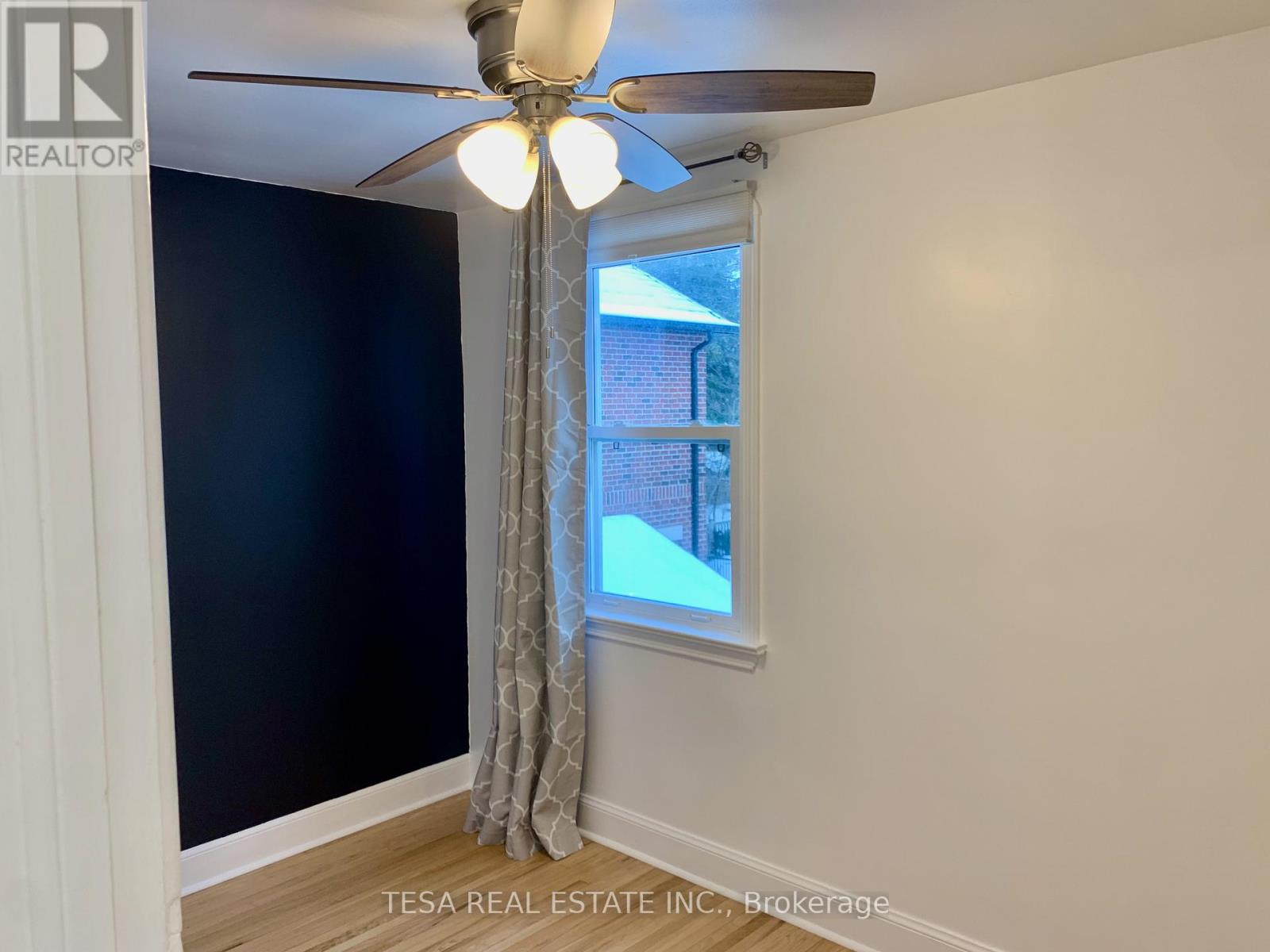 A room with a ceiling fan and a window showing a view of a building outside.