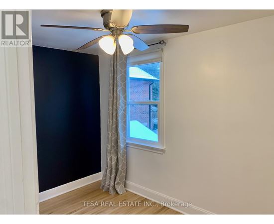 A room with a ceiling fan and a window showing a view of a building outside.