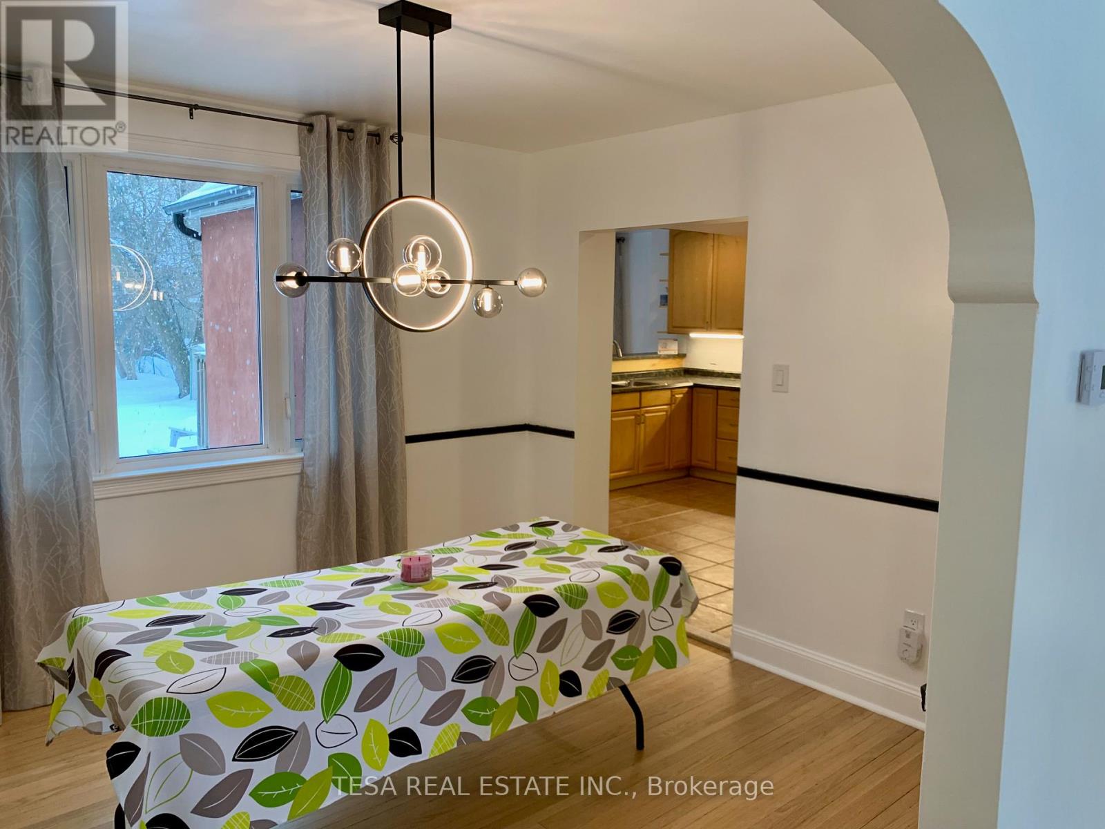 A dining table with a green leaf pattern cloth is in the middle of a room with a kitchen in the background.