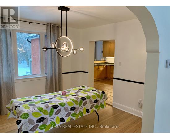 A dining table with a green leaf pattern cloth is in the middle of a room with a kitchen in the background.