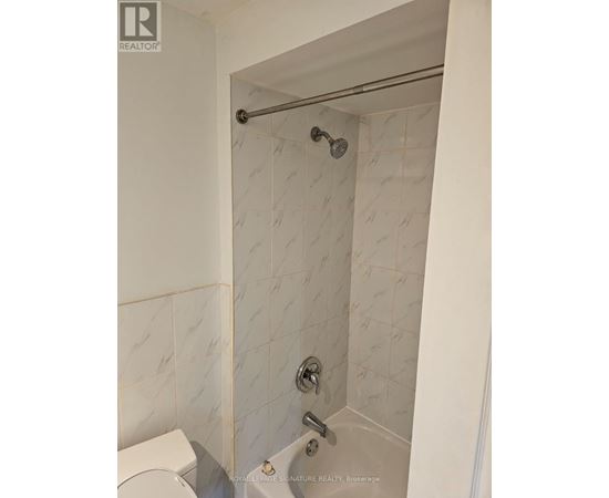 A white tiled shower with a glass door and a silver shower head.
