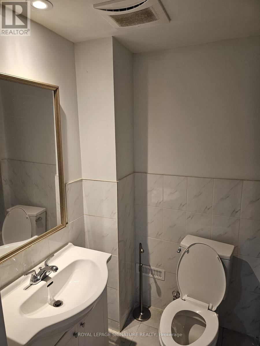 A white toilet is in a bathroom with a sink and mirror.