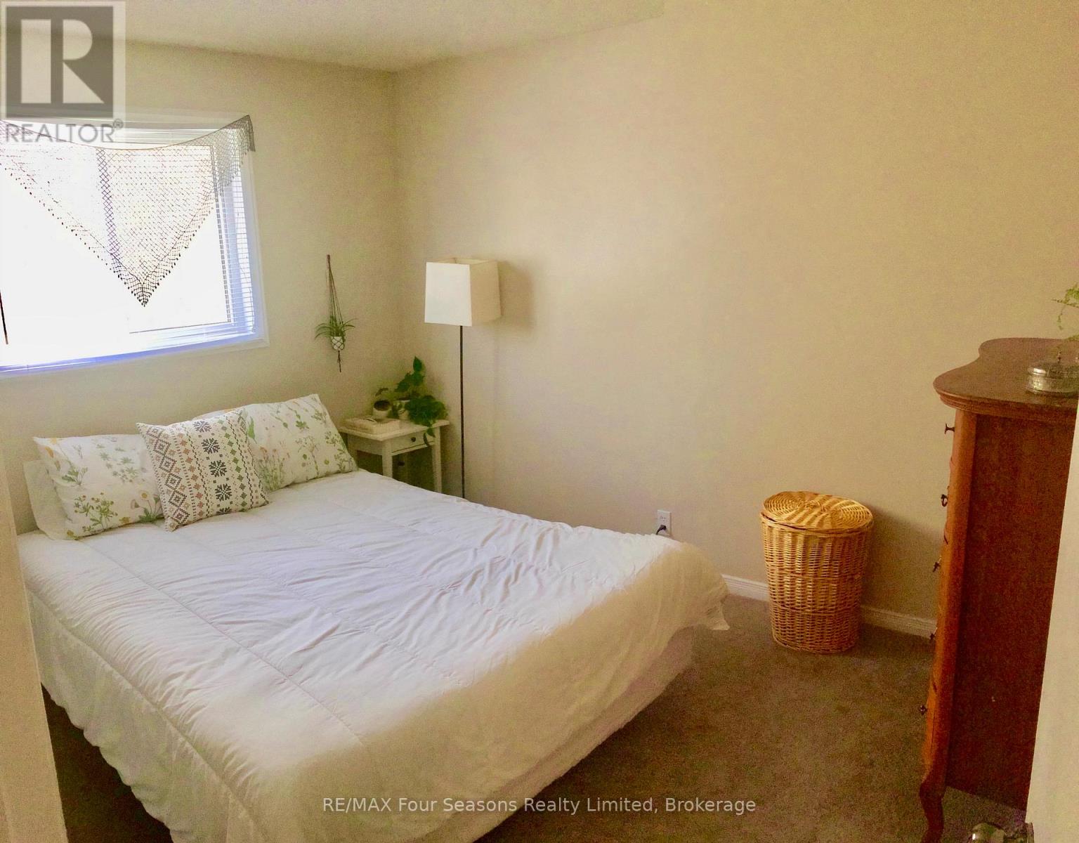 A bedroom with a bed, nightstand, and a window with a plant on it.