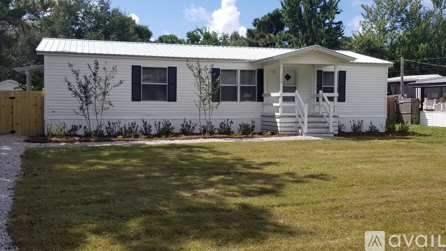A white mobile home with a porch and a small tree in front.