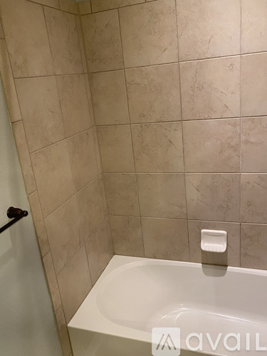 A bathroom with a white tub and beige tiled walls.
