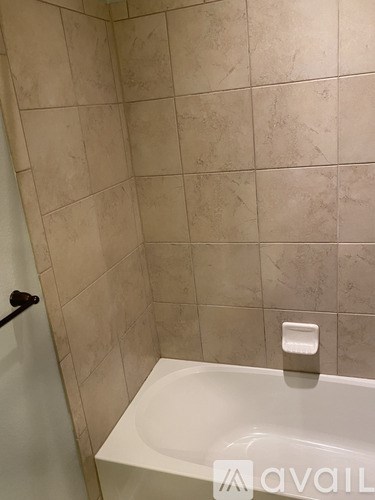 A bathroom with a white tub and beige tiled walls.