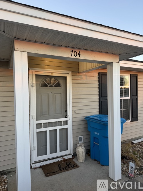 A house numbered 704 has a blue trash bin and a mat on the porch.