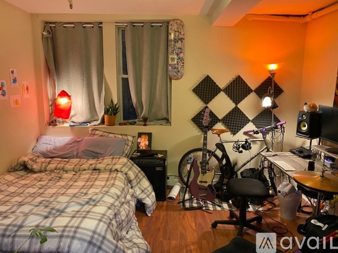 A room with a bed, a desk with a computer, a guitar, a bicycle, and a lamp.
