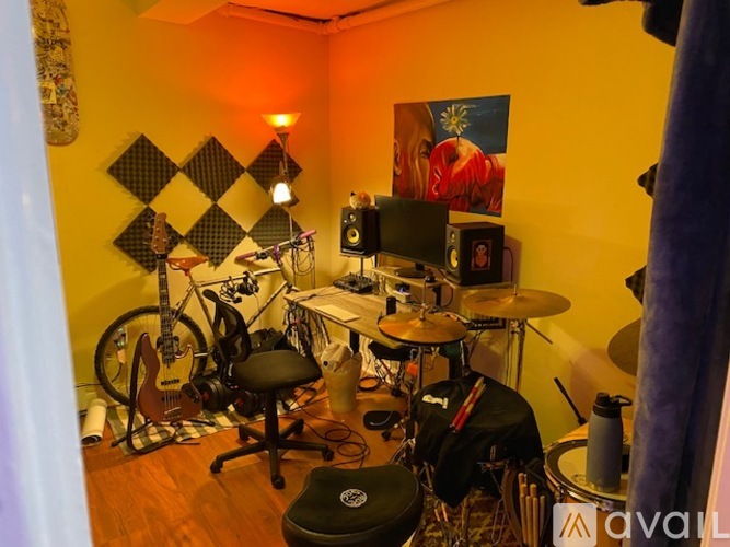 A room with a drum set, a guitar, a bicycle, and a checkered wall.