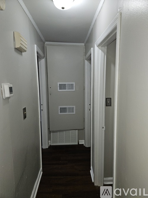 A long hallway with a door on the right and a wall-mounted thermostat on the left.