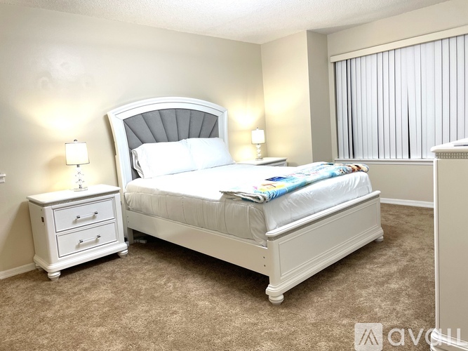 A white bedroom with a large bed and a nightstand with two lamps.