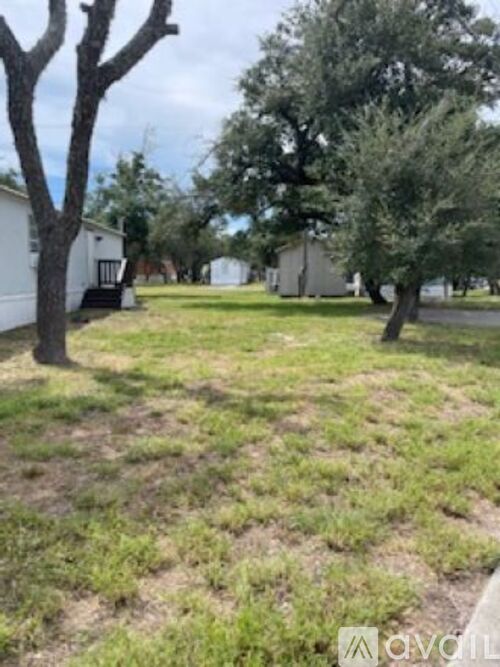 A grassy area with trees and a white building in the background.