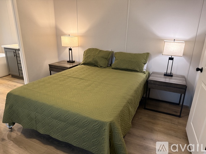 A bed with a green cover and two matching pillows sits in a room with two lamps on either side.