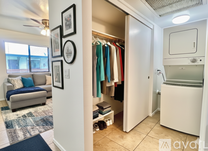 A room with a couch, a fan, and a wall with pictures and a closet with clothes.