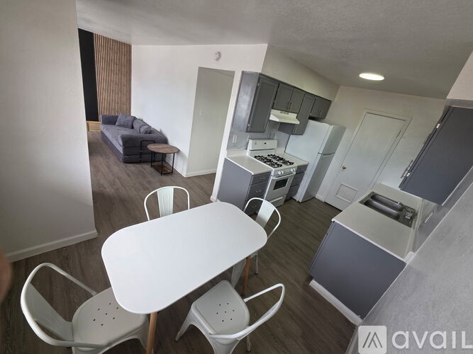 A kitchen area with a table and chairs in the foreground and a refrigerator, microwave, and oven in the background.