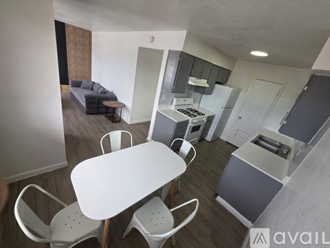 A kitchen area with a table and chairs in the foreground and a refrigerator, microwave, and oven in the background.