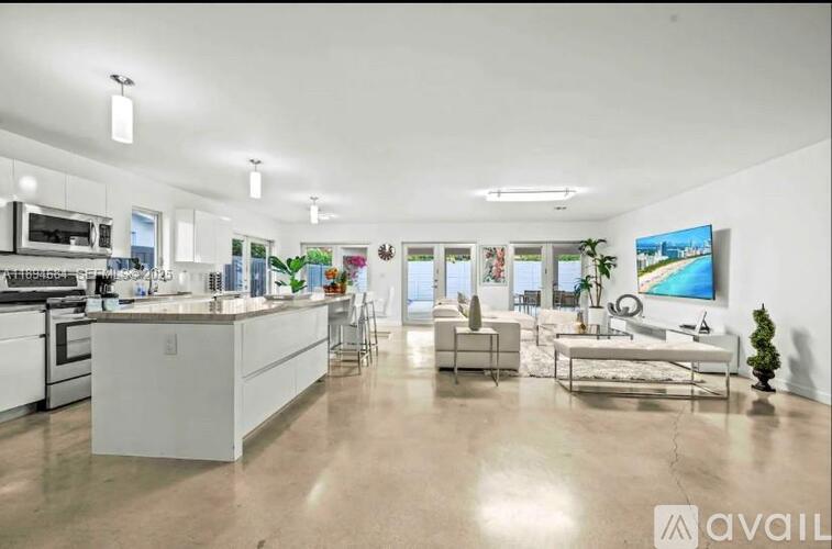 A modern kitchen with white cabinets and appliances, a dining table with chairs, and a large TV mounted on the wall.