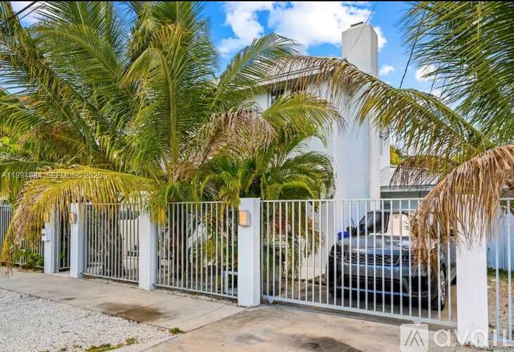 A white house is surrounded by a metal fence and palm trees.