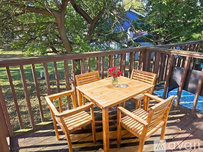 A wooden table with chairs is on a deck with a pool in the background.