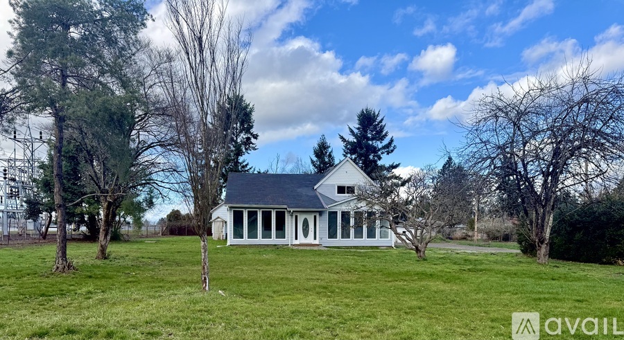 A white house with a black roof is surrounded by trees and grass.