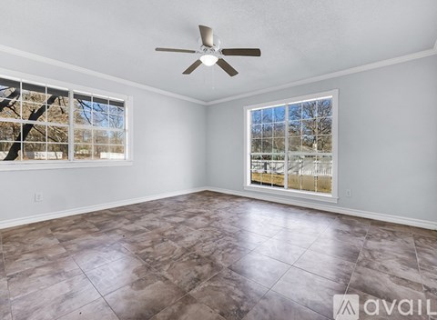 A room with a ceiling fan and a large window with a view of trees and a fence.