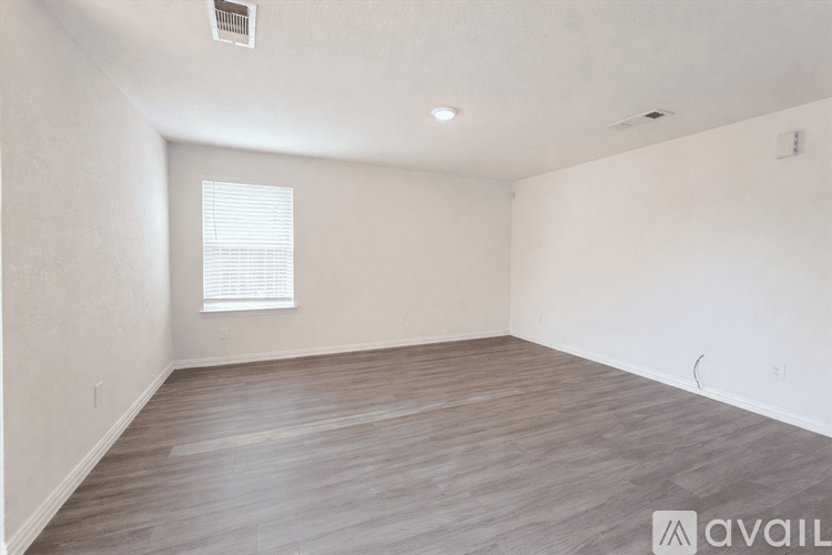 A spacious room with wooden flooring and a window with blinds.