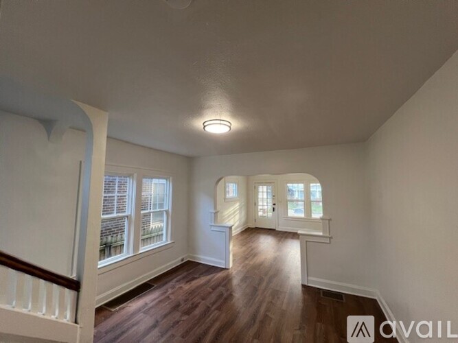 A spacious room with wood flooring and white walls.