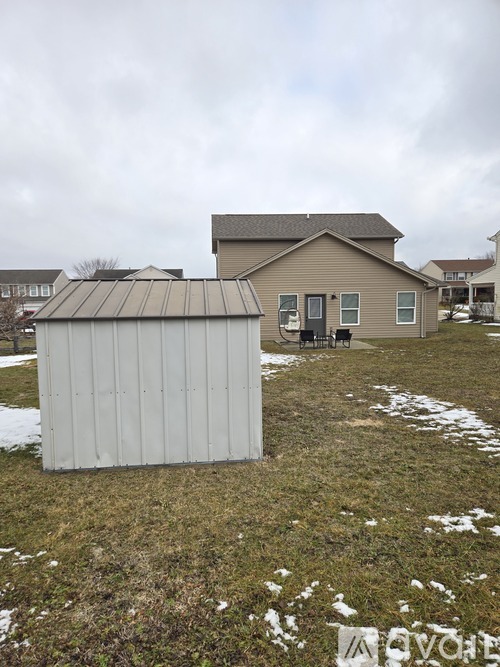A shed sits in a grassy field with a house in the background.