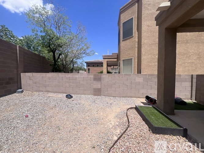 A backyard with a wall, a hose, and a small patch of grass.