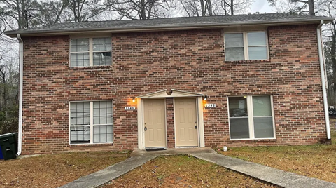 A brick house with a brown door and two windows.