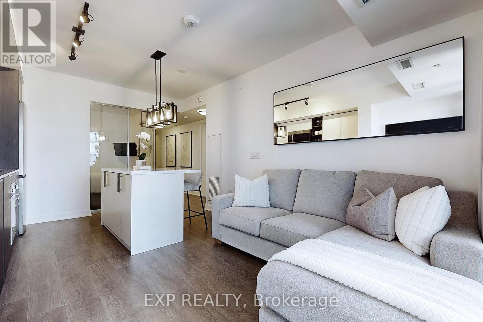 A modern living room with a grey couch and a white kitchen area.