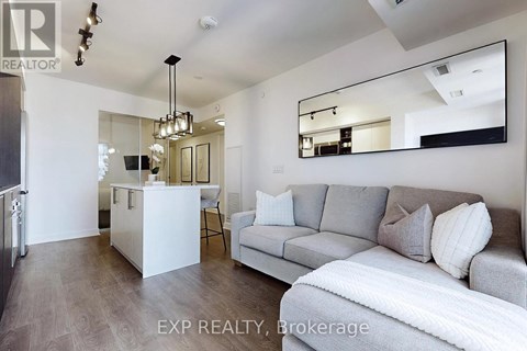 A modern living room with a grey couch and a white kitchen area.