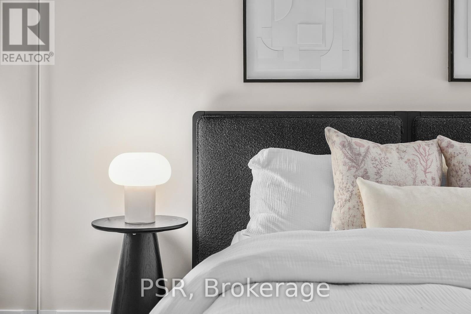 A modern bedroom with a large bed and a side table with a lamp.