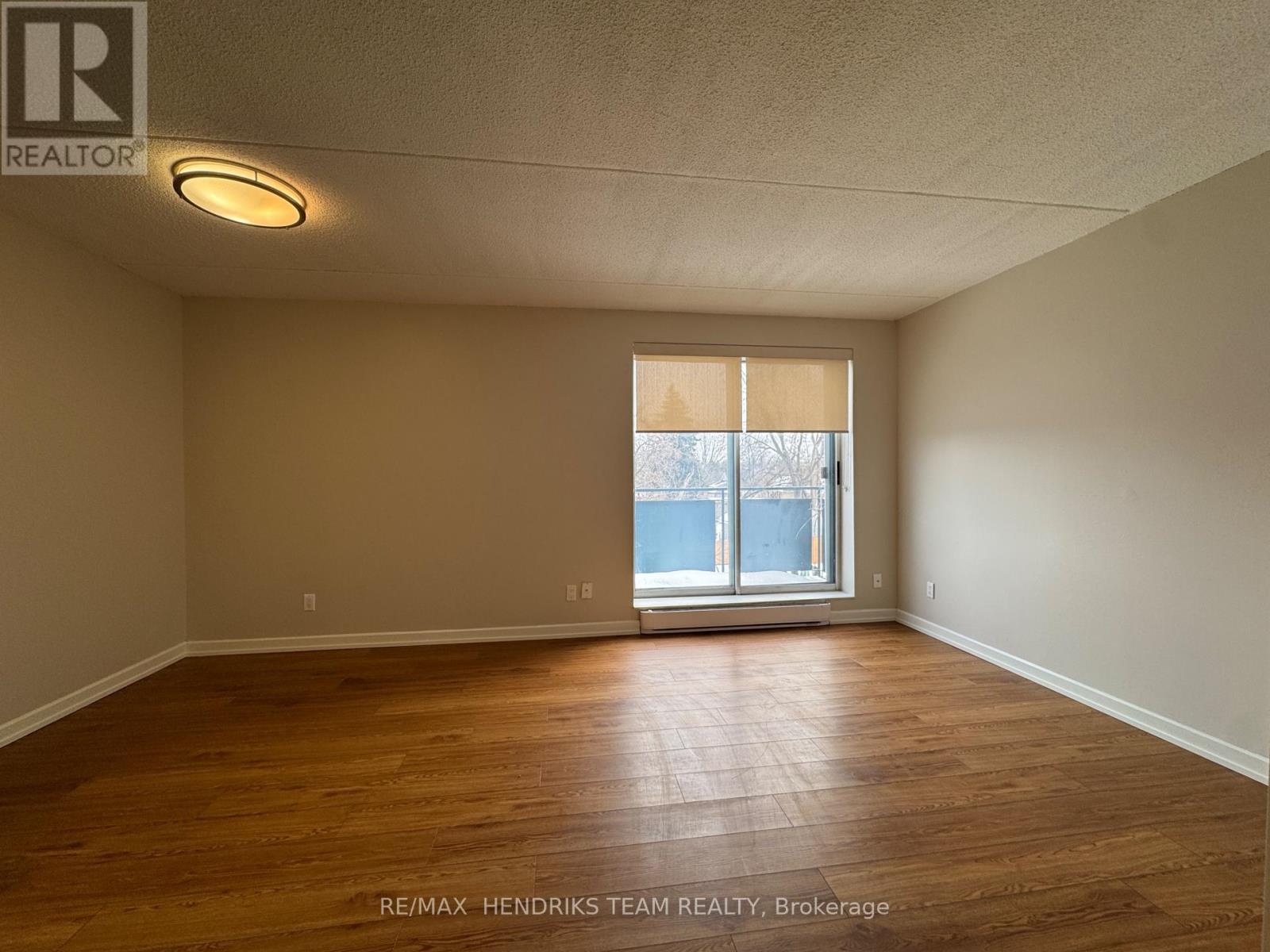 A spacious room with wooden flooring and a window with blinds.